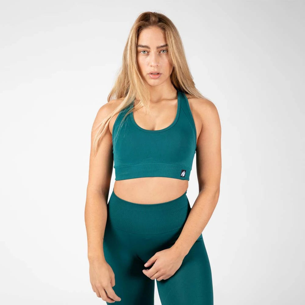 Gorilla Wear Yava Seamless Sport Bra Green, en sömlös grön sport-bh med bred ribbad linning buren av en kvinna.