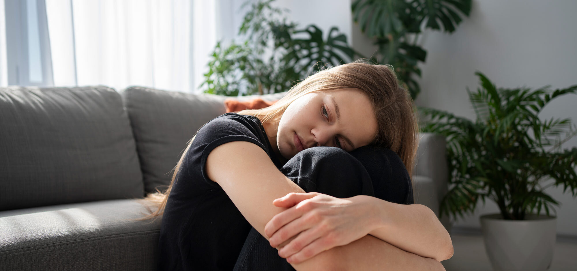 En ung kvinna sitter hopkrupen i soffan med ett trött och nedstämt uttryck, vilket illustrerar symtom på postcovid. I artikeln diskuteras kreatin som en möjlig hjälp, med fokus på psykisk och fysisk återhämtning.