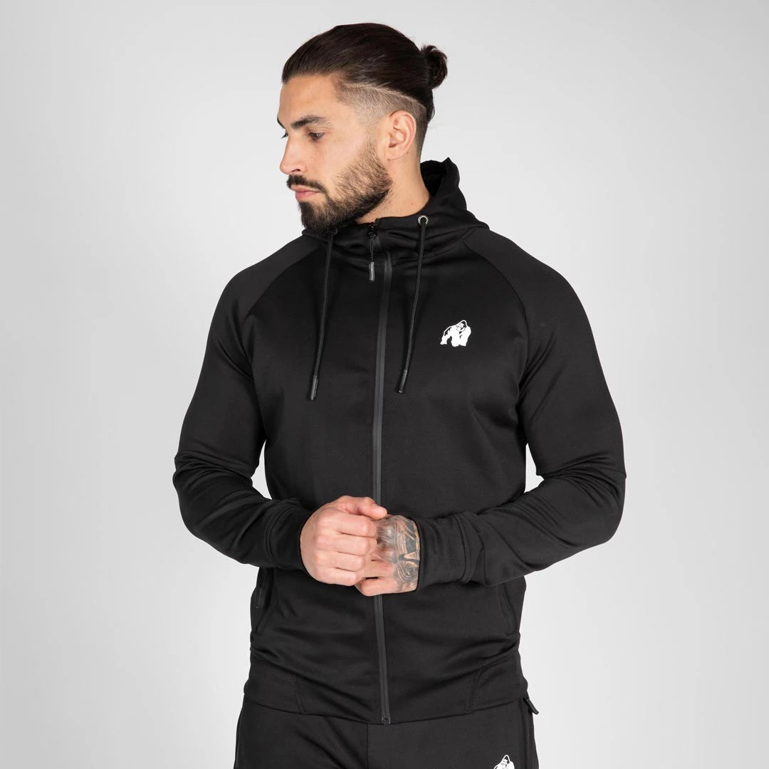Gorilla Wear Sullivan Track Jacket Black, en svart träningsjacka med huva och vit logotyp buren av en man., bild 6 av 7