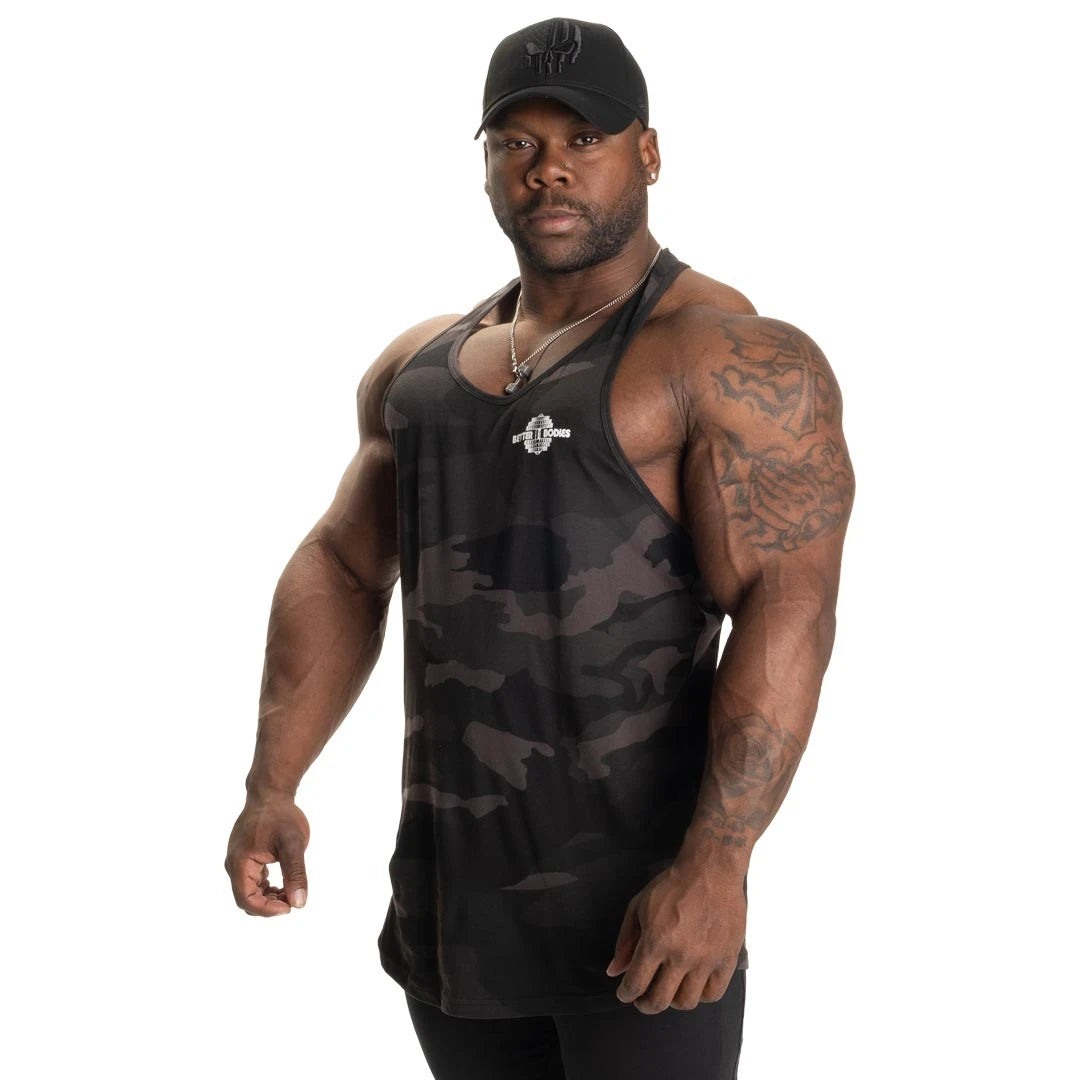 Better Bodies Essential T-back V2 Dark Camo träningslinne i mörkt kamouflagemönster och mjuk bomull, buret av en man., bild 4 av 6