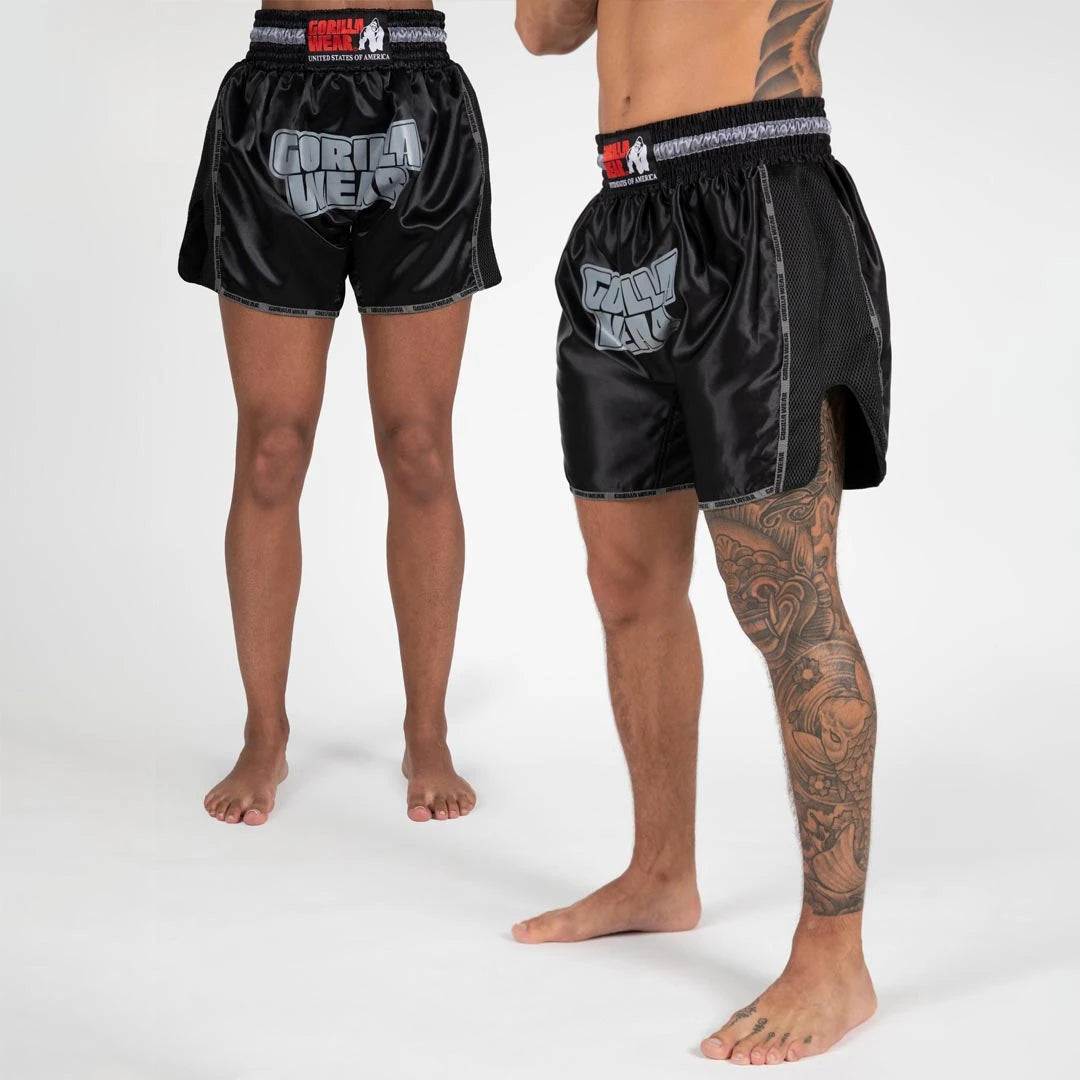 Gorilla Wear Piru Muay Thai Shorts black i glansigt material med stor grå logotyp, sidoslitsar och elastisk midja.