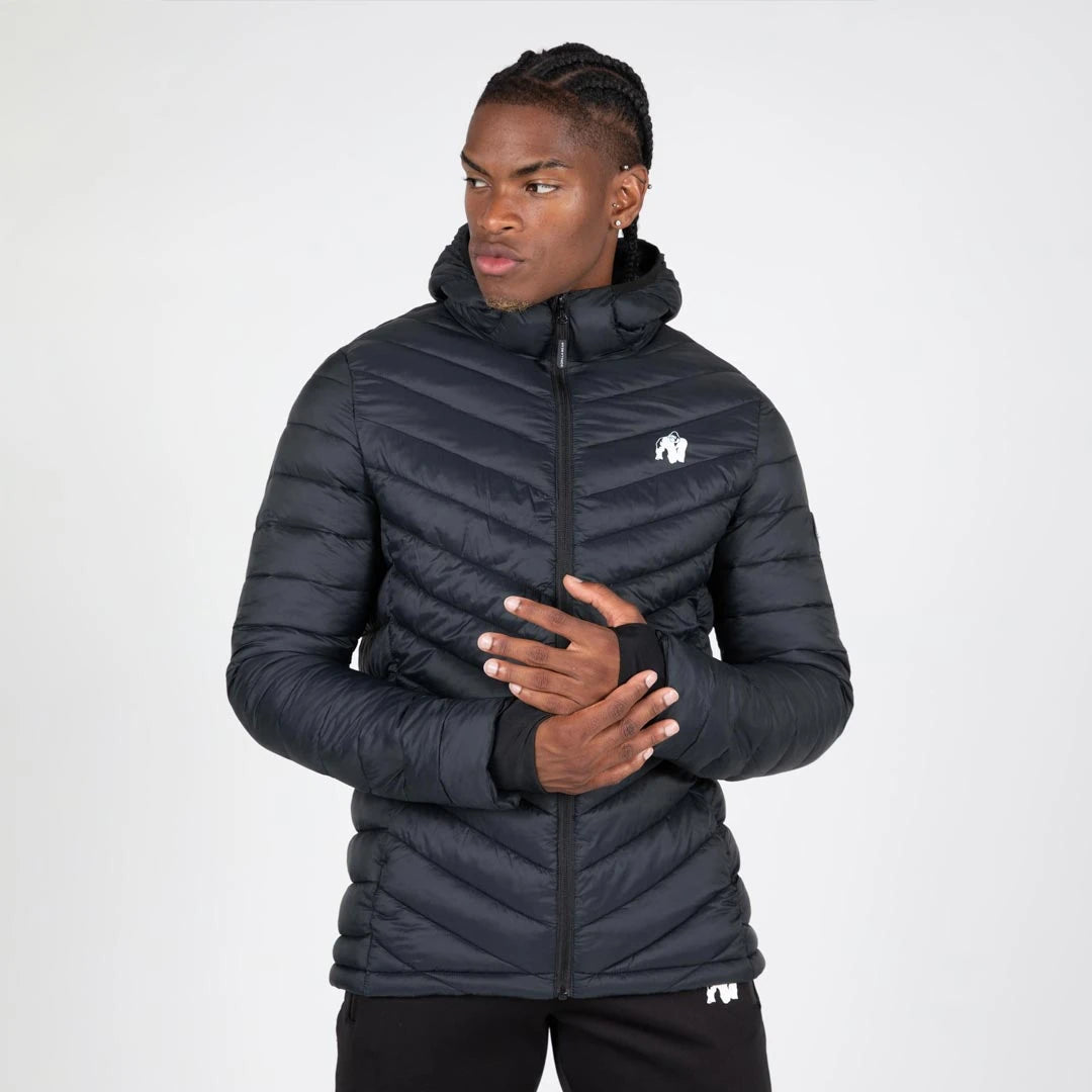 Gorilla Wear Osborn Puffer Jacket Black, en svart vadderad nylonjacka med huva och tumhål, buren av en man., bild 3 av 8