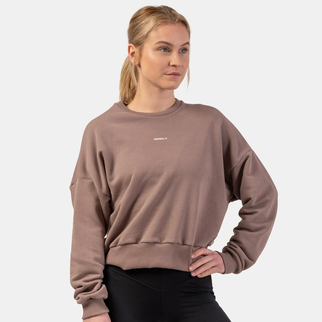 NEBBIA Loose Fit Sweatshirt Feeling Good Brown, en brun träningströja med lös passform och breda muddar buren av en kvinna., bild 2 av 3