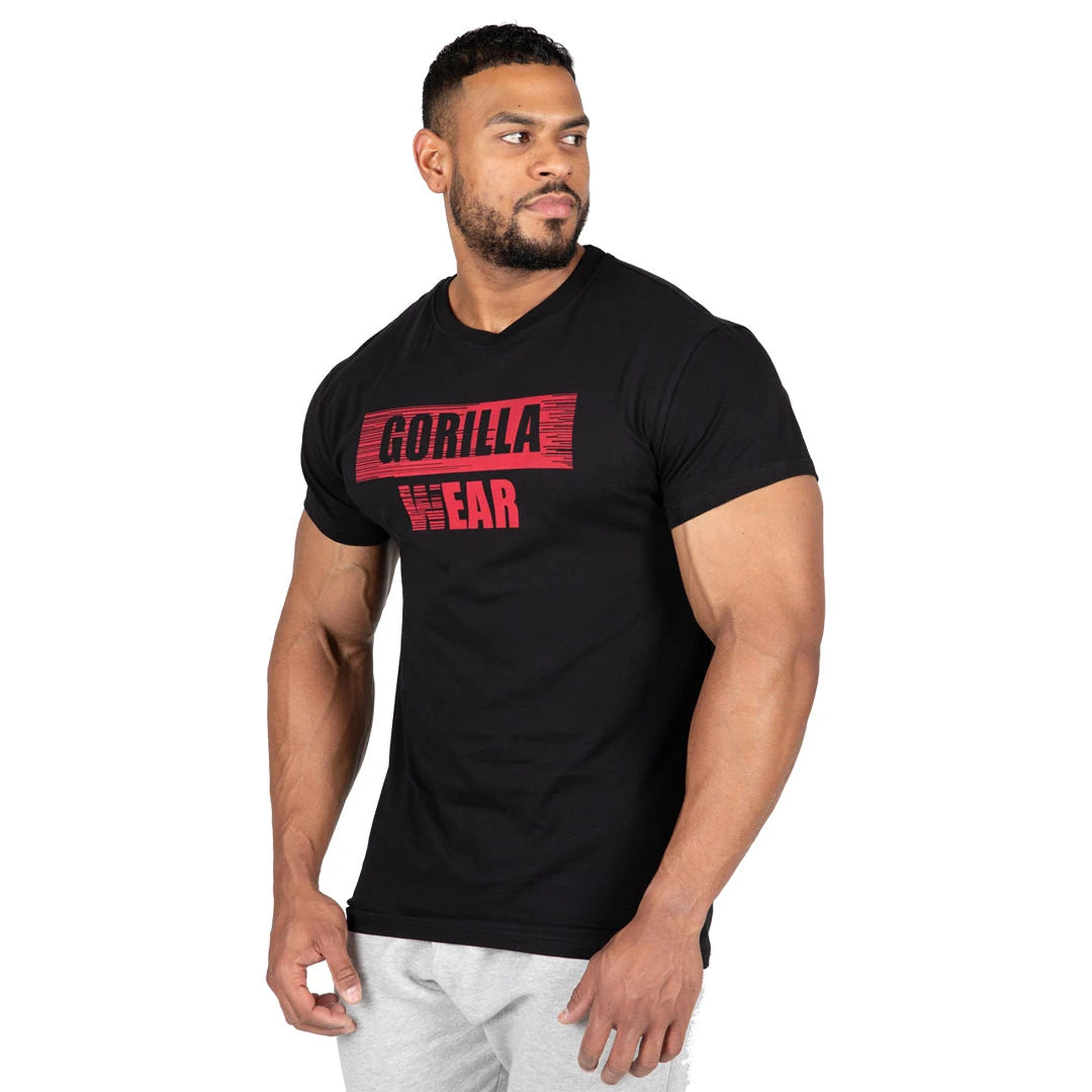 Gorilla Wear Murray T-Shirt Black i svart bomull med slim fit och rött logotryck, buren av en man.