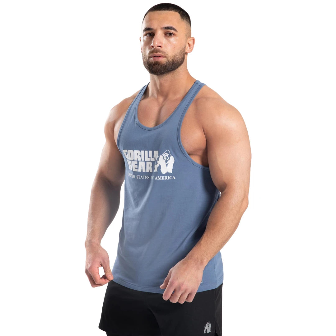 Gorilla Wear Classic Tank Top Coronet Blue, ett blått träningslinne i mjuk bomull med vitt tryck buret av en man., bild 1 av 7