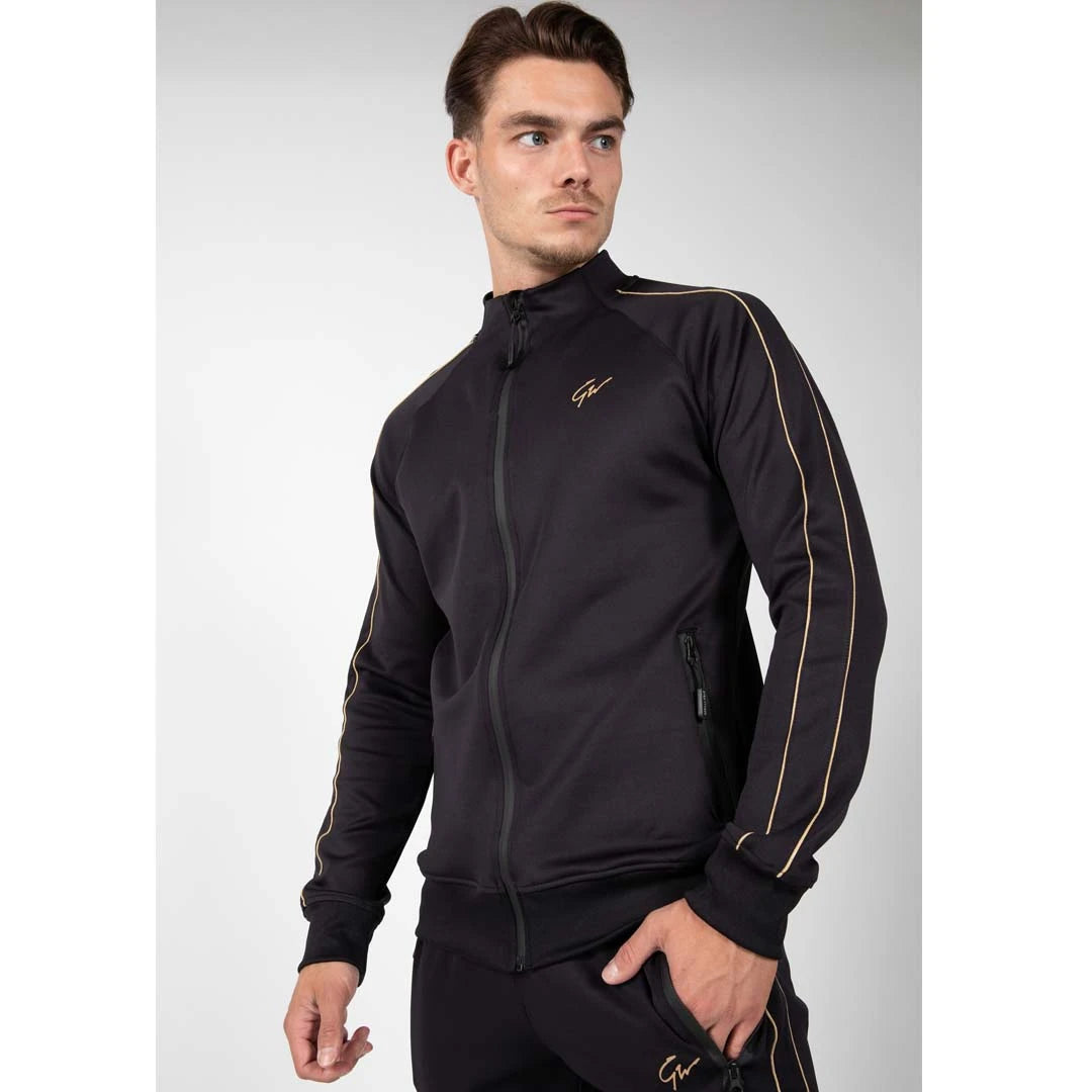 Man i Gorilla Wear Wenden Track Jacket Black/Gold, en svart träningsjacka med gulddetaljer och dragkedja., bild 4 av 8