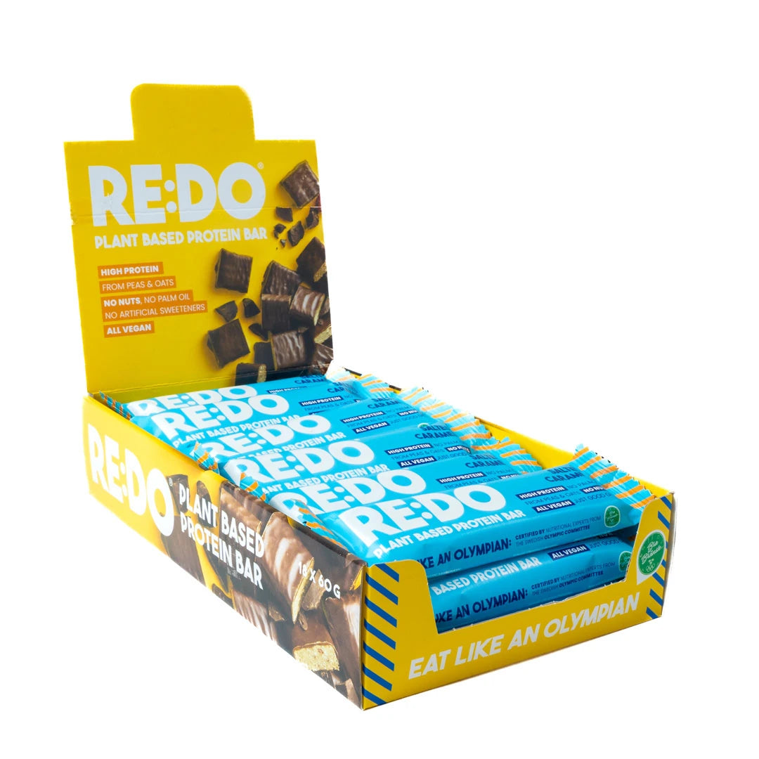 18 x REDO Bar 60 g Salty Caramel i en gul displaylåda med blåa proteinbars.