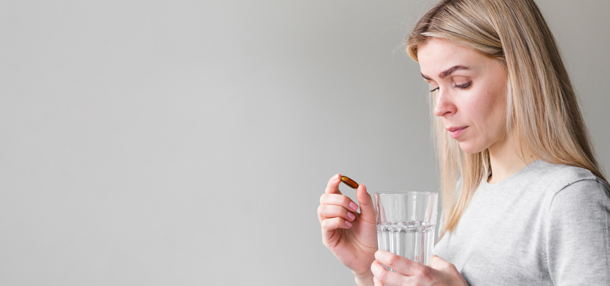 En kvinna i grå tröja håller ett glas vatten och en brun kapsel med krom, ett mineral som kan bidra till att balansera blodsockernivåer och stödja ämnesomsättningen.