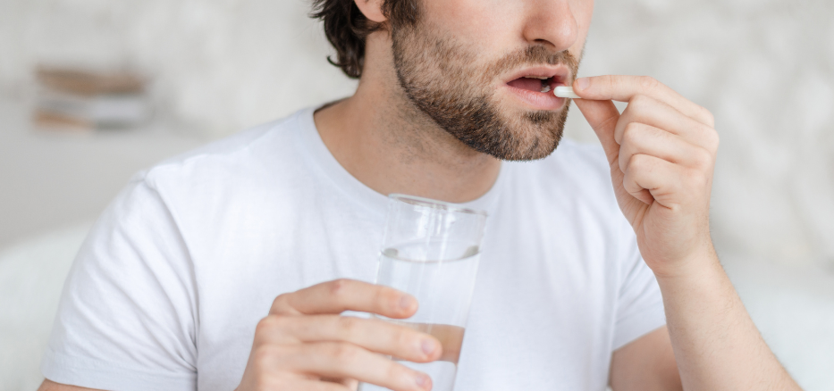 Man som håller i ett glas med vatten och tar vitamintillskott